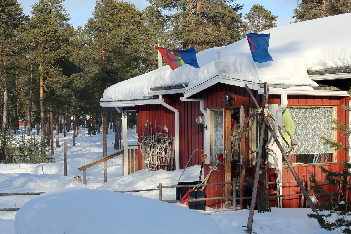 Red wooden cabin with snow-covered roof and reindeer antlers on the wall
