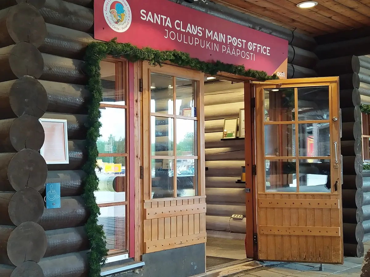 Log-wall entrance of the Santa Claus Main Post Office with wreaths and red sign