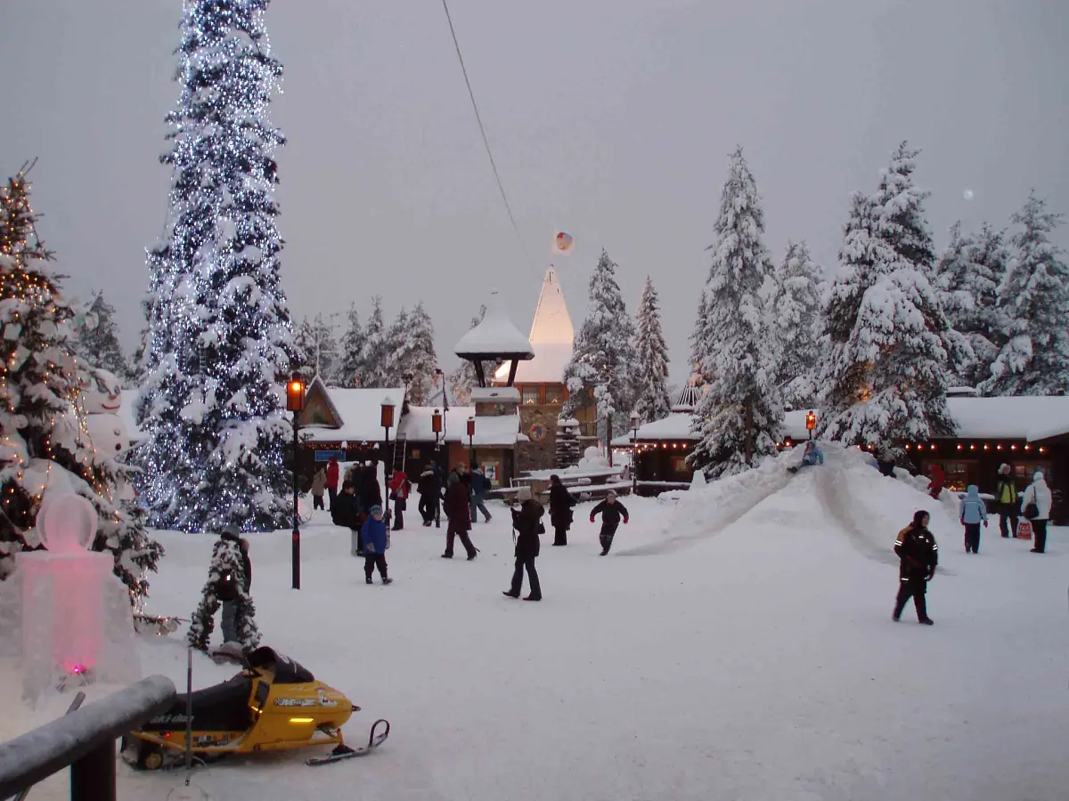 Snow-covered square with small wooden houses and frosted fir trees at Santa Claus Village