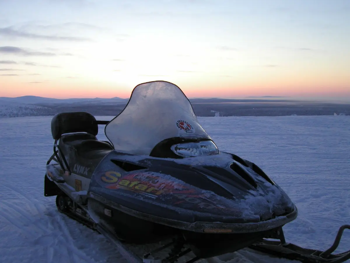 Snowmobile parked on a snowy plain at sunset in Lapland